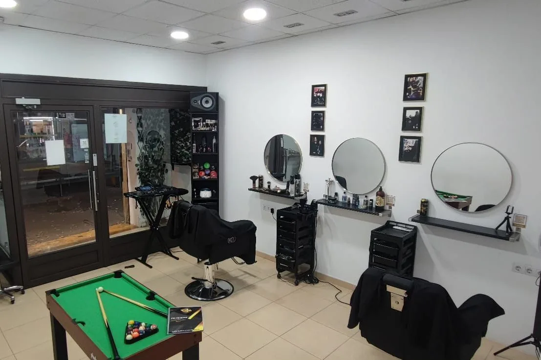 Vista general de Più Eleganza: sillones de barbero, espejos redondos, cuadros y mesa de billar en la zona de espera